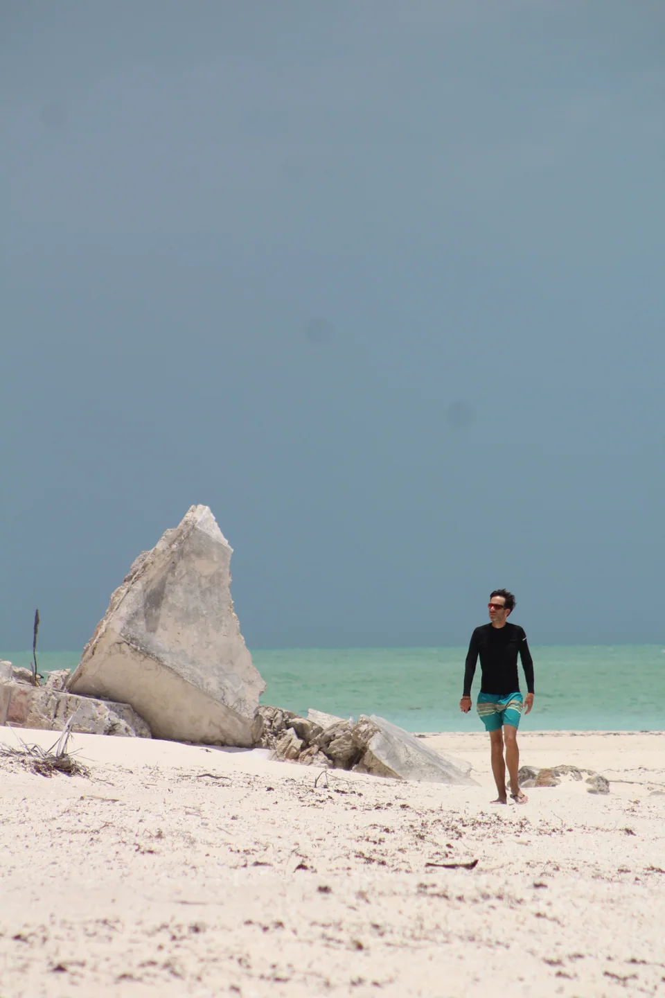Hombre caminando por la playa de Holbox junto a una gran roca
